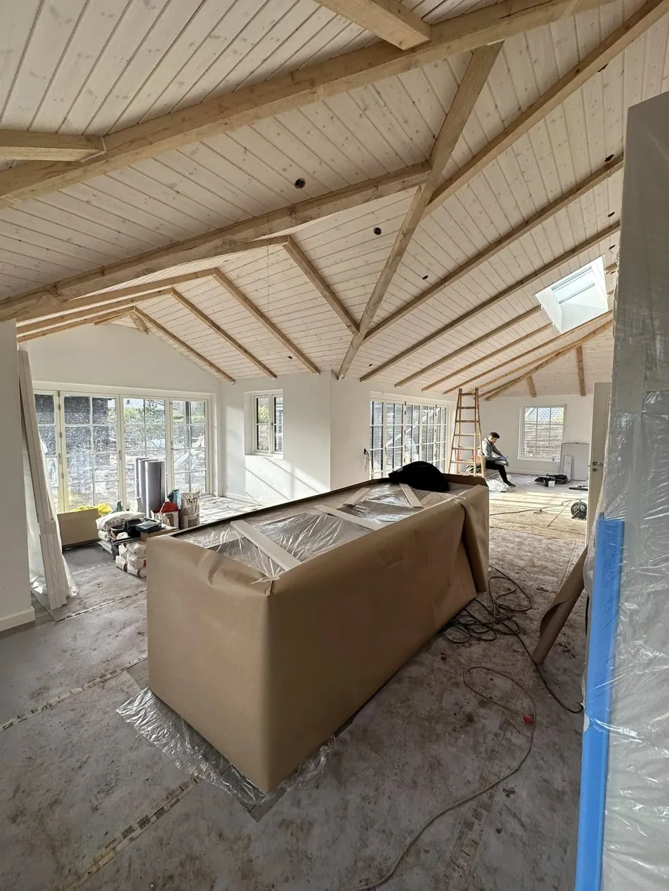 Stort rum under totalrenovering med åben tagkonstruktion og afdækning